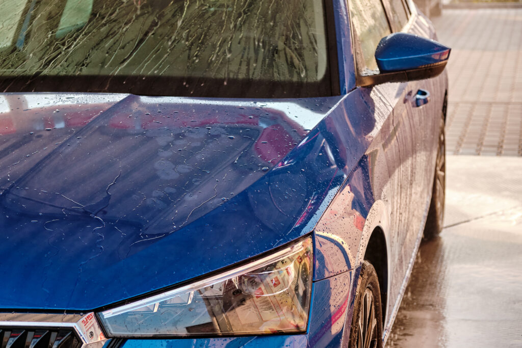 Close up hood and headlight of a blue car in a drops of water after car washing. Clean car after high pressure water washing