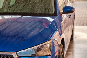 Close up hood and headlight of a blue car in a drops of water after car washing. Clean car after high pressure water washing