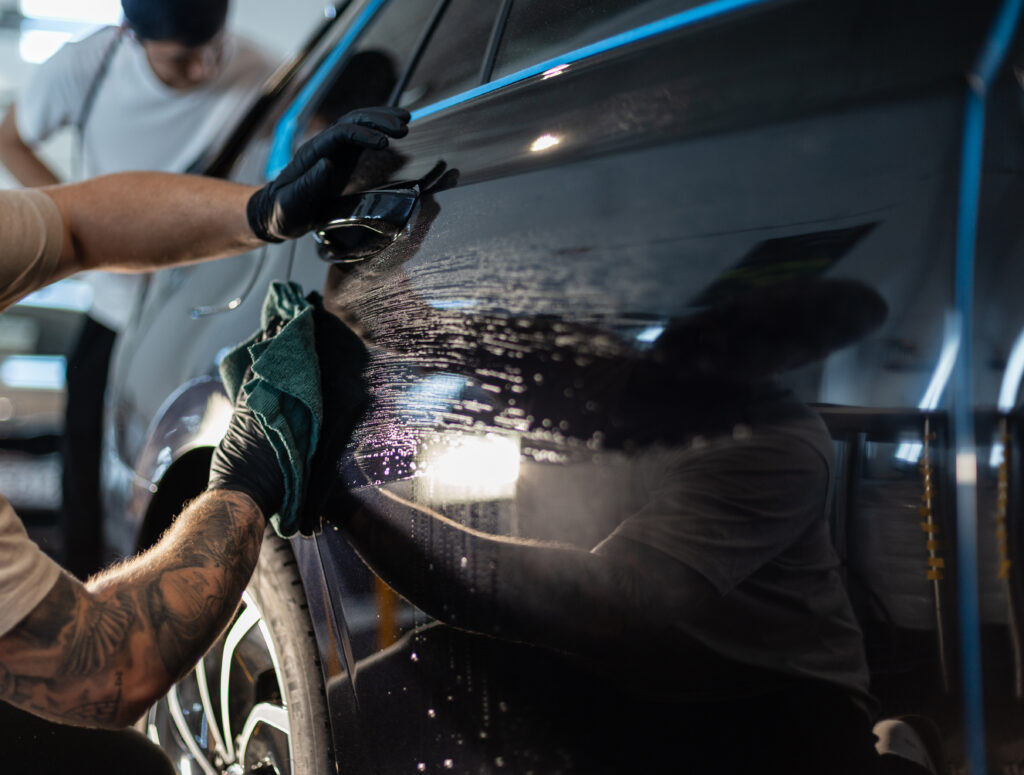 Man car washer washes car and wipes black car with rag in detailing studio