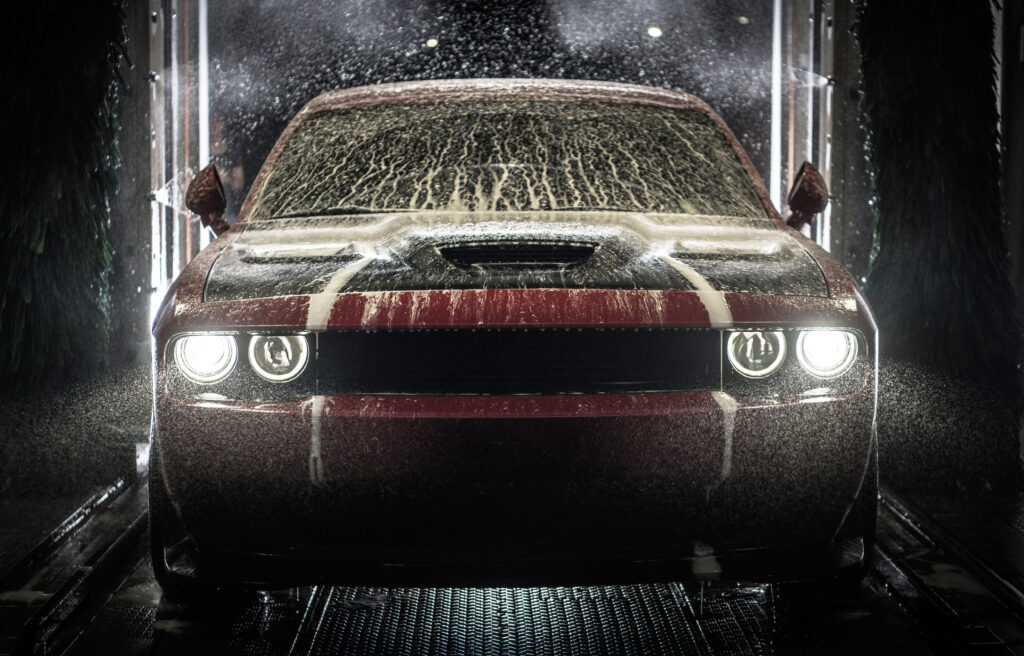 A red car gets washed under strong water spray and soap in a wash station at night.