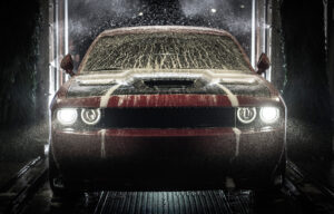 A red car gets washed under strong water spray and soap in a wash station at night.