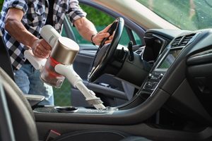 Man uses handheld vacuum cleaner to clean center console of car interior. Modern car interior cleaning and maintenance
