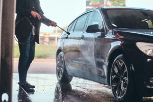 Busy man in jeans and blaser is washing his own car at car washing station.
